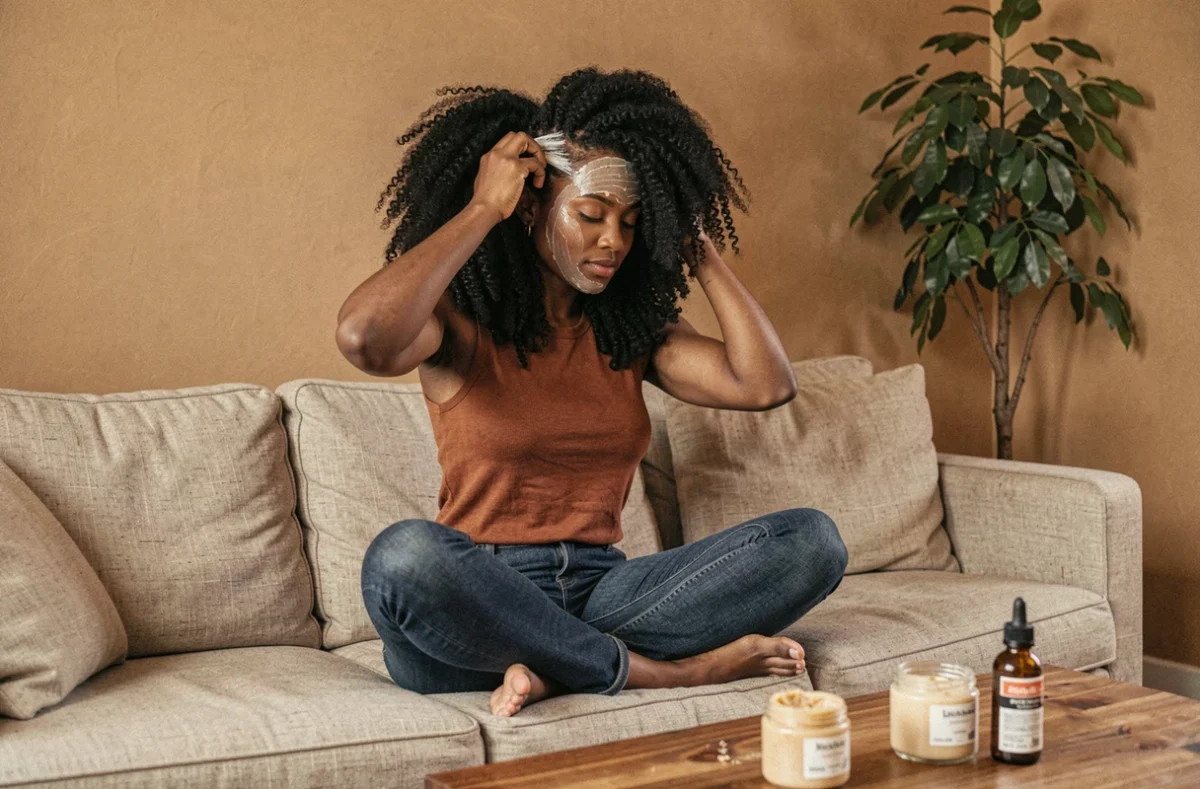 Jeune femme aux cheveux crépus appliquant un masque hydratant sur ses cheveux naturels dans un salon chaleureux